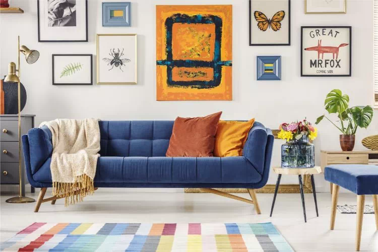 Canapé bleu avec une multitude de tableaux au mur derrière lui