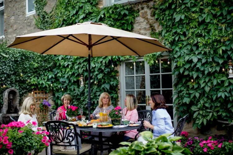 Amies autour d'une table sous un parasol, sur une terrasse devant une maison